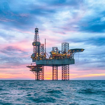 Offshore oil rig platform in the ocean at sunset with a colorful sky.