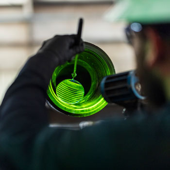 Worker inspecting the inside of a pipe with a UV light, revealing fluorescent green markings.