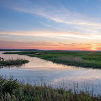 Serene coastal marsh landscape with winding waterway and sunset sky.